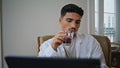 Serious guy enjoying cocktail at home close up. Relaxed man watching laptop