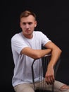 A serious guy, sitting on a chair, leaning his hands on the back of the chair. On a black background. Royalty Free Stock Photo