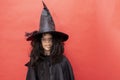 serious Halloween kid. Child in black sorcerer's costume. Witch cheerfully looks at the camera on red background