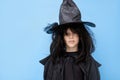 serious Halloween kid. Child in black sorcerer& x27;s costume. Witch cheerfully smiles and looks at the camera on blue