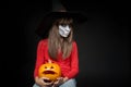 Serious Halloween witch holding Jack O`Lantern pumpkin looking at camera