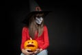 Serious Halloween witch holding Jack O`Lantern pumpkin looking at camera