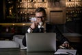 Serious handsome elegant caucasian businessman sitting at restaurant working on his laptop and drinking coffee