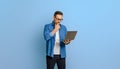 Serious handsome entrepreneur touching chin and doing research over laptop against blue background