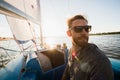 Serious handsome young male yacht captain in sunglasses wearing gloves staying on boat deck and looking into distance