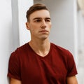 Serious handsome young man in a fashionable red t-shirt with a stylish hairstyle is standing outdoors near a vintage white Royalty Free Stock Photo