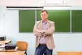 The serious headmaster stands in the classroom at the blackboard with his arms folded Royalty Free Stock Photo