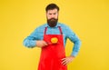 Serious hipster in cook apron hold ripe tomato on sharp knife yellow background, snacking