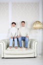 Serious husband and wife sits on back of white leather sofa