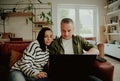 Serious husband and wife using laptop at home browsing while sitting together on sofa