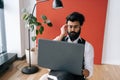 Serious Indian business man in formalwear working typing on laptop sitting soft poof in light coworking office by window Royalty Free Stock Photo