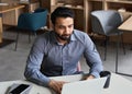 Serious indian business man working with laptop and cellphone in remote office.