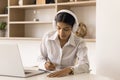 Serious Indian company intern woman in wireless headphones writing notes Royalty Free Stock Photo