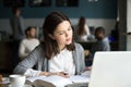 Serious intelligent millennial girl studying in cafe preparing f