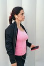 Serious Latina woman listening to music while standing near wall on city street during workout Royalty Free Stock Photo