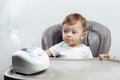 Serious little baby boy sitting on the high chair an using nebulizer. Baby health care concept.