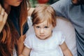 Serious little blonde girl sitting between mon and dad in the garden. Portrait of the child with her young parents. Love and Royalty Free Stock Photo