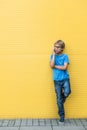Serious little boy talking on cell phone standing near yellow wall outdoors Royalty Free Stock Photo