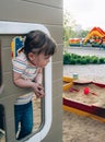 Serious little girl peeking out of a small house on the playground Royalty Free Stock Photo