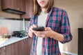 Serious long-haired young man standing in the kitchen uses his mobile phone to write SMS or order a service from the Royalty Free Stock Photo
