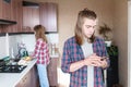 Serious long-haired young man standing in the kitchen uses his mobile phone to write SMS or order a service from the Royalty Free Stock Photo