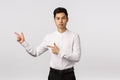Serious-looking asian businessman give direction, pointing left, recommend visit site link, look corporate banner Royalty Free Stock Photo