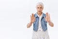 Serious-looking fed up angry senior woman with combed grey hair, raise hands in stop, taboo or refusal motion, frowning