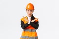 Serious-looking fed up asian female boss, construction manager in safety helmet showing cross gesture to stop, prohibit
