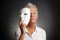 Serious older woman revealing face behind mask