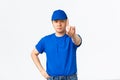 Serious-looking reluctant asian courier in blue uniform forbid something, disapprove behaviour or action, shaking finger
