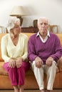 Serious Looking Senior Couple Sitting On Sofa At Home