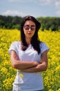 Serious lovely brunette in sunglasses stay in rapeseed field. Spring.
