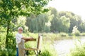 Serious male artist holding brush and painting picture on easel on open air. Royalty Free Stock Photo