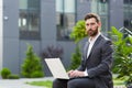 Serious male businessman working on laptop at lunchtime sitting on bench near office in business suit Royalty Free Stock Photo