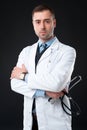 Serious male doctor holds stethoscope in hand isolated on black Royalty Free Stock Photo