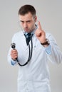 Serious male doctor holds stethoscope in hand and pointing finger Royalty Free Stock Photo