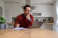 Serious male freelancer writing notes while doing research over wireless computer on desk at home