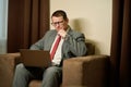 Serious male in glasses sits with laptop on his knees