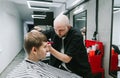 Serious male hairdresser creates a stylish hairstyle for a young client. Barber cuts hair on the head of a handsome guy. Barber