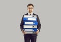 Serious male office worker standing on gray background holding stack of large folders for documents. Royalty Free Stock Photo