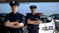 Serious male officers standing with hands crossed against police car background