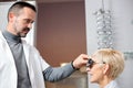 Serious male optometrist examining mature woman, determining diopter in ophthalmology clinic