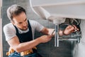 Serious male plumber in working overall fixing sink