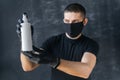 Serious Man in a black protective mask and gloves holds a white antiseptic in his hands. Prevention of coronovirus and epidemic.