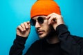 Serious man on blue background. Wearing round sunglasses and orange hat. Royalty Free Stock Photo