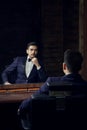 Serious man in blue suit and butterfly sitting in chair looking in the mirror in barbershop Royalty Free Stock Photo