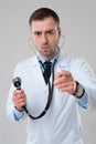 Serious man doctor holds stethoscope in hand and pointing at cam Royalty Free Stock Photo