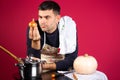Serious man holding a onion in the kitchen. Photo on a pink background. The concept of gender stereotypes