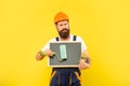 serious man renovator in helmet and work clothes hold paint roller brush and blackboard