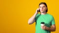 Serious man with a sad expression, talking on a cell phone, drinking coffee to go, wearing a green t-shirt Royalty Free Stock Photo